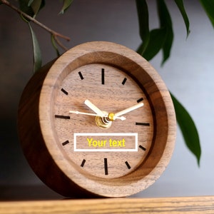 May include: A wooden clock with a gold-colored face and hands. The clock has black Roman numeral markings and the text "Your text" on the face.