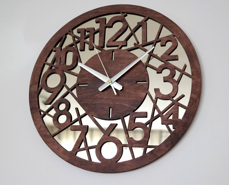 May include: A brown wooden clock with a mirrored face and black numbers. The numbers are cut out of the wood and the mirror is visible behind them. The clock hands are silver.