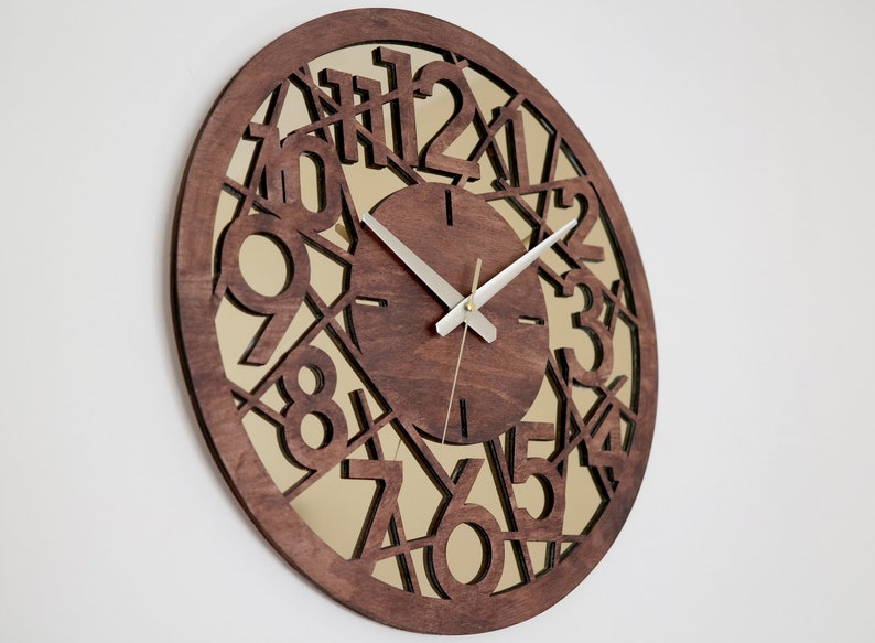 May include: A brown wooden wall clock with a mirrored face. The clock face has a geometric design with the numbers 1 through 12 cut out. The clock hands are silver.