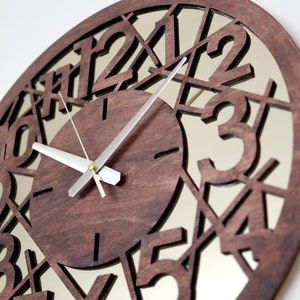 May include: A brown wooden clock with a mirrored face. The numbers 1 through 12 are cut out of the wood and the clock hands are silver.
