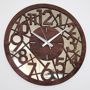 May include: A brown wooden clock with a mirrored face. The numbers 1 through 12 are cut out of the wood and the mirror is visible behind them. The clock hands are silver.