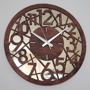 May include: A brown wooden clock with a mirrored face. The clock face has a unique design with the numbers 1 through 12 cut out and arranged in a circular pattern. The clock hands are silver.