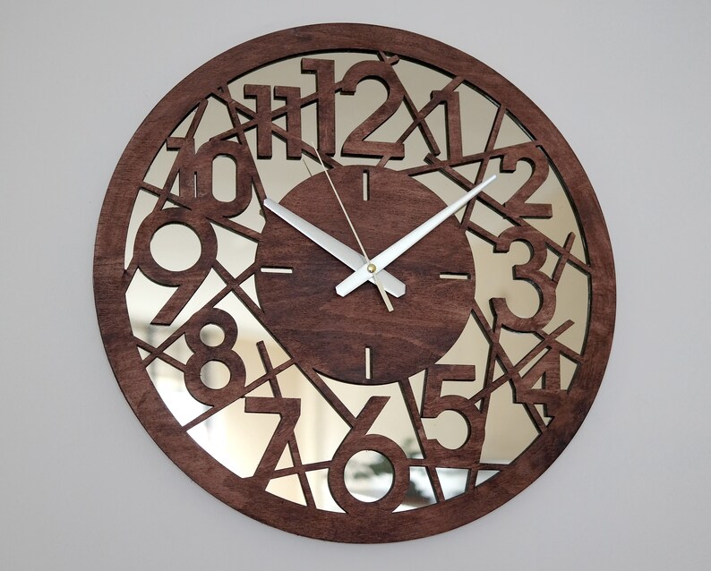 May include: A brown wooden clock with a mirrored face. The clock face has a unique design with the numbers 1 through 12 cut out and arranged in a circular pattern. The clock hands are silver.