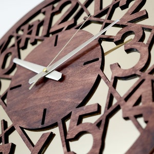 May include: A brown wooden clock with a mirrored face and silver hands. The clock face has numbers cut out of the wood, creating a unique design.