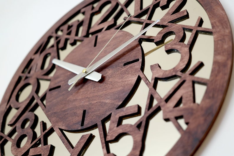 May include: A brown wooden clock with a mirrored face and silver hands. The clock face has numbers cut out of the wood, creating a unique design.