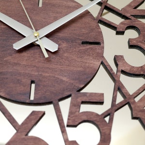 May include: A brown wooden clock with a mirrored face. The numbers 1, 2, 3, 4, and 5 are cut out of the wood and are visible through the mirror. The clock hands are silver.