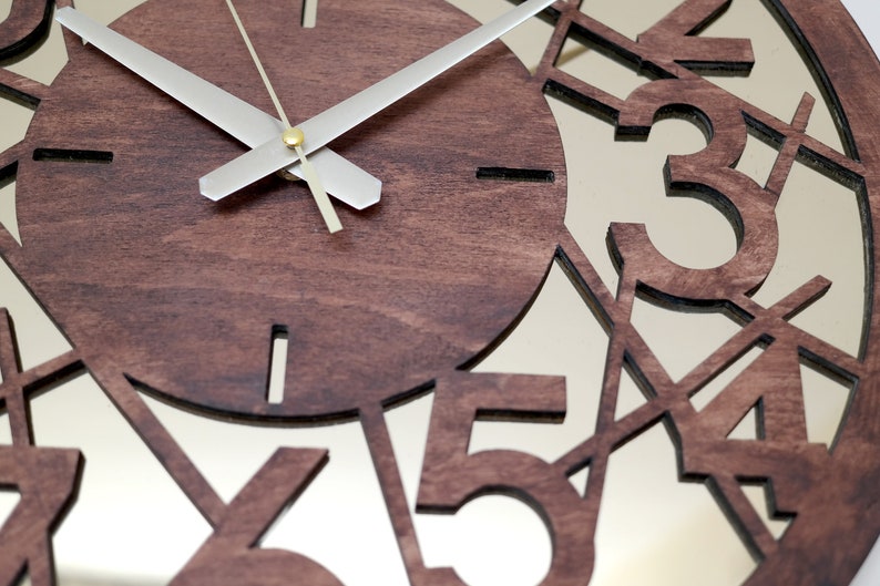 May include: A brown wooden clock with a mirrored face. The numbers 1, 2, 3, 4, and 5 are cut out of the wood and are visible through the mirror. The clock hands are silver.