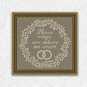 Könnte beinhalten: Ein gerahmtes Kreuzstichbild mit dem Text "These rings are where we start" in einem Kranz aus Blättern und zwei ineinandergreifenden Ringen. Der Rahmen ist braun und der Hintergrund ist neutral. Unten steht "INSTANT DOWNLOAD PDF".