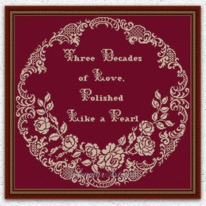Könnte beinhalten: Kreuzstichmuster mit burgunderfarbenem Hintergrund und einem weißen floralen Design. Das Muster zeigt den Text "Three Decades of Love, Polished Like a Pearl".