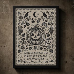 May include: A framed cross-stitch sampler on beige fabric featuring a central jack-o'-lantern, crows, pumpkins, corn, and mushrooms in black thread. The design includes a crescent moon, stars, and the full alphabet in a gothic-style font.
