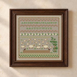 May include: A framed cross-stitch sampler featuring a gray background with the alphabet in green, rows of red and white flowers, and a pastoral scene with white sheep, a brown wooden fence, a green tree, and two small birds at the bottom.