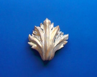 May include: A gold-colored metal leaf design with a textured surface. The leaf is on a blue background.