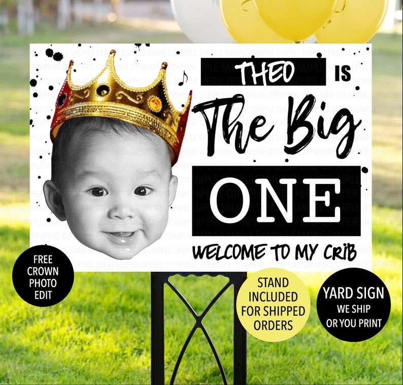 May include: Black and white yard sign with a photo of a baby wearing a gold crown. The sign says "Theo is the big one, welcome to my crib".