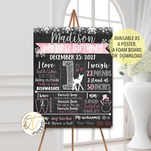 May include: A chalkboard style first birthday sign with a pink and white snowflake design. The sign says "Madison My First Birthday December 25, 2021". It includes details about the child's weight, height, favorite things, and nicknames.