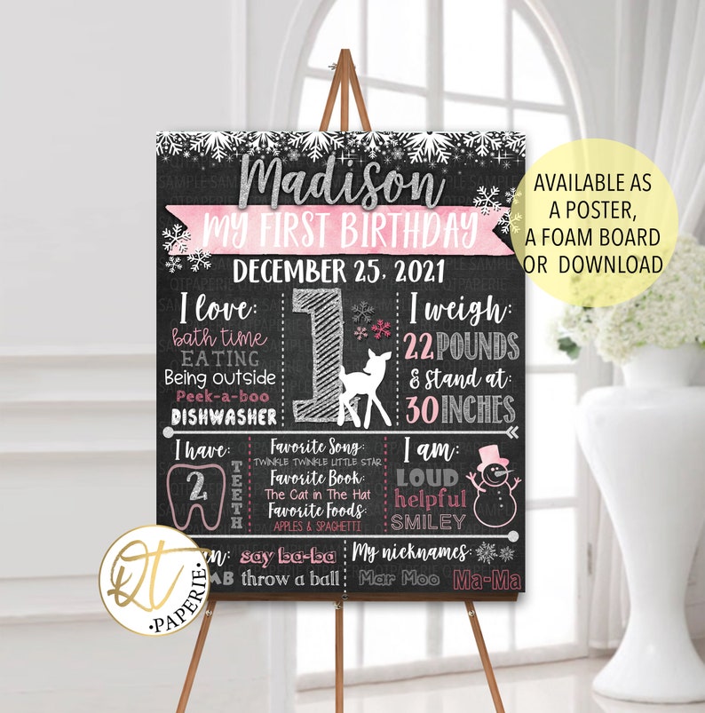 May include: A chalkboard style first birthday sign with a pink and white snowflake design. The sign says "Madison My First Birthday December 25, 2021". It includes details about the child's weight, height, favorite things, and nicknames.