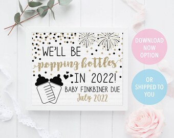 May include: A white framed printable announcement with gold glitter text that reads "We'll be popping bottles in 2022! Baby Finkbiner due July 2022". The announcement features black and gold confetti and black fireworks.