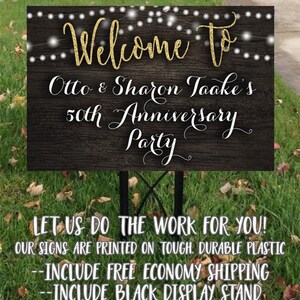 May include: A black and gold welcome sign with string lights for Otto & Sharon Taake's 50th Anniversary Party. The sign is printed on durable plastic and includes a black display stand.