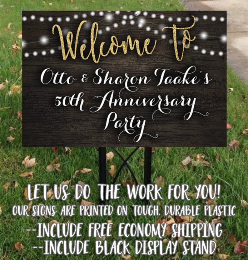 May include: A black and gold welcome sign with string lights for Otto & Sharon Taake's 50th Anniversary Party. The sign is printed on durable plastic and includes a black display stand.