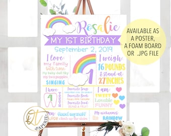 May include: A colorful rainbow-themed first birthday sign for a girl named Rosalie. The sign includes details like her weight (16 pounds), height (27 inches), favorite song, book, and food. It also includes a cute illustration of a tooth and the text "I have 4 teeth".