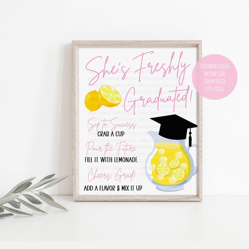 May include: A framed print with the text "She's Freshly Graduated!" in pink script. The image includes illustrations of lemons, a pitcher of lemonade with a graduation cap, and instructions for making lemonade. A pink circle says "Download Now or Shipped to You."