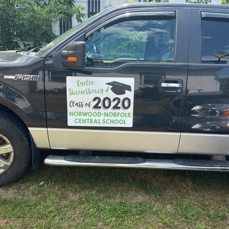 May include: A black pickup truck with a white sign on the side that says "Kailee Shrewsbury Class of 2020 Norwood-Norfolk Central School". The sign has a green graduation cap and a green border.