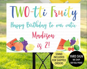 May include: A white yard sign with the text "TWO-tti Fruity" in colorful letters. Below, it reads "Happy Birthday to our cutie Madison is 2!" with fruit illustrations. A black stand supports the sign.