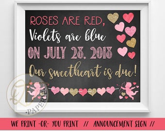 Puede incluir: Cartel de pizarra enmarcado con el texto "Roses are red, violets are blue, on July 28, 2018, Our sweetheart is due!" en letras rosas y doradas. El cartel incluye decoraciones de corazones rosas y dorados y una ilustración de cupido rosa.