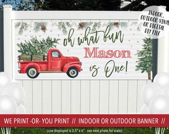 Puede incluir: Un camión rojo con un árbol de Navidad en la parte trasera, una pancarta verde y blanca con el texto "oh what fun Mason is One!" y una valla de madera blanca en el fondo. La pancarta mide 6,35 cm por 15,24 cm.