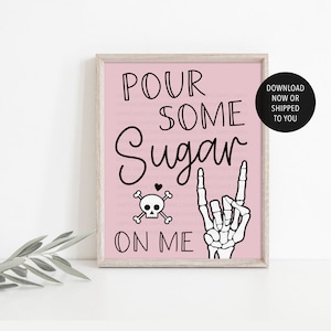 May include: A pink framed print with the text "Pour some sugar on me" in black. A skull and crossbones with a heart above it is to the left of the text. A skeleton hand with a rock and roll hand gesture is to the right of the text.