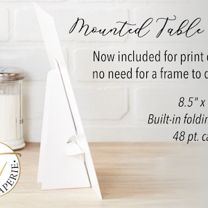 May include: White table sign with a built-in folding stand. The sign is 8.5 inches by 11 inches and is made of 48 pt. cardstock. The text on the sign reads "Mounted Table Sign" and "Now included for print orders - no need for a frame to display!"