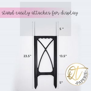May include: Black metal stand with a 23.5 inch height, 13.5 inch width, and 5 inch depth. The stand has a decorative design and is used for displaying items.
