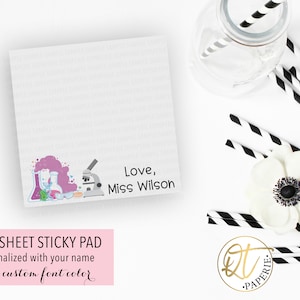 May include: A white sticky note pad with a science theme. The pad has a pink and blue illustration of beakers, a microscope, and a test tube. The text "Love, Miss Wilson" is printed on the pad. The pad is 50 sheets and can be personalized with your name and custom font color.