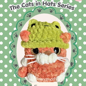May include: A crochet plush toy named Frogger from The Cats in Hats Series. The orange cat features a green frog hat, large glittery black eyes, white whiskers, and white paws. The background is green with white polka dots and includes text.