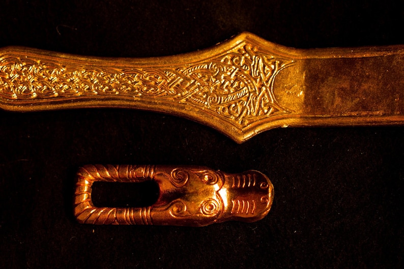 Puede incluir: Dos piezas de metal de color dorado con dise&ntilde;os intrincados. La pieza m&aacute;s grande es una forma rectangular larga y plana con un extremo redondeado y un patr&oacute;n decorativo. La pieza m&aacute;s peque&ntilde;a es una forma ovalada curva con un agujero en el centro.