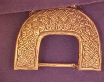 May include: A large, ornate, gold-toned metal belt buckle with an intricate woven design.