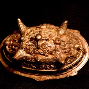 Könnte beinhalten: Eine verzierte, ovale Brosche in Gold mit filigranen Details und einer erhabenen, strukturierten Mitte.