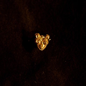 Puede incluir: Un amuleto de búho de metal dorado con detalles intrincados.