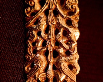 Op de afbeelding: Een gouden metalen hanger met een ingewikkeld ontwerp met twee vogels met uitgespreide vleugels. De hanger heeft een rechthoekige vorm met een platte bovenkant en een afgeronde onderkant. Het ontwerp is gedetailleerd en ingewikkeld, met de veren van de vogels en andere details duidelijk zichtbaar.