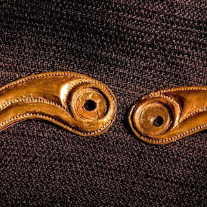 May include: Two gold-colored metal pieces with intricate designs, each featuring a curved shape with a series of circular holes. The pieces are likely decorative elements for a larger object.