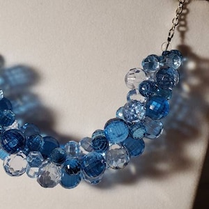 May include: A silver chain necklace with a graduated ombre design of clear, light blue, and dark blue faceted glass beads.