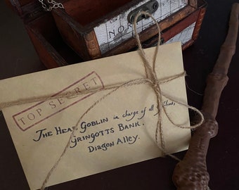 May include: A brown wooden chest with a map design, a silver locket, and a wand. A tan envelope tied with twine has the words "TOP SECRET" and text about Gringotts Bank.