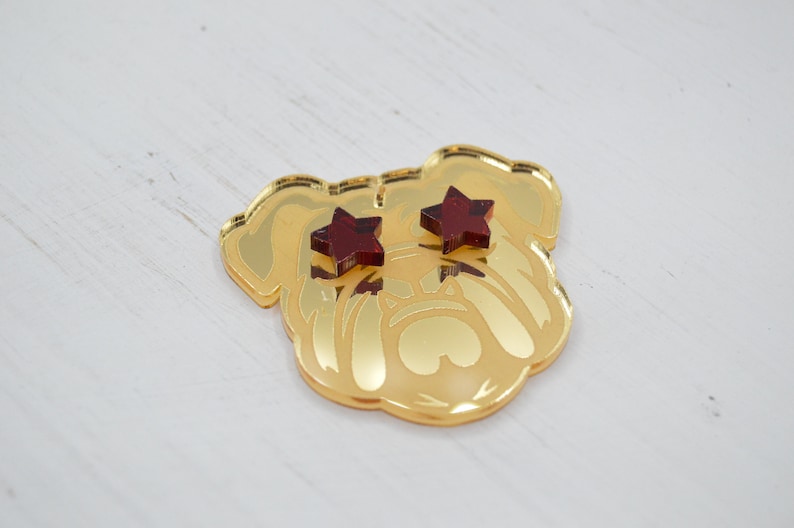 Pu&ograve; includere: Testa di bulldog in specchio dorato con occhi a forma di stella rossa.