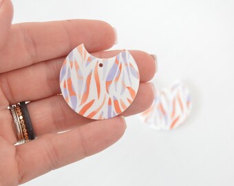 May include: A pair of white, orange, and purple patterned resin earrings with a hole for a hook or wire.