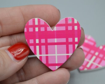Può includere: Due ornamenti in legno a forma di cuore a quadri rosa e bianchi con un foro in alto per appendere.