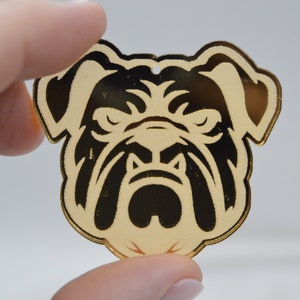 Pu&ograve; includere: Ciondolo in acrilico color oro con la testa di un bulldog nero e bianco.