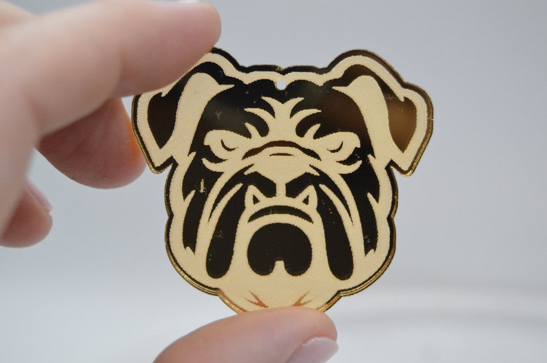 Pu&ograve; includere: Ciondolo in acrilico color oro con la testa di un bulldog nero e bianco.