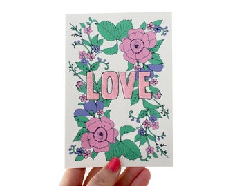 May include: A card with a floral design featuring pink and purple flowers and green leaves. The word "LOVE" is written in pink letters in the center of the card.