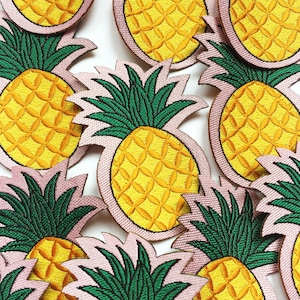 May include: A collection of embroidered pineapple patches with pink and green accents. The pineapples are yellow with a detailed pattern.