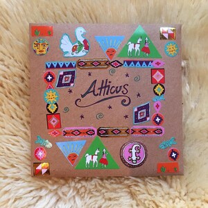 Pu&ograve; includere: Un sacchetto regalo di carta marrone con adesivi colorati. Gli adesivi raffigurano un uccello, un lama, un sole, uno schema geometrico e la parola "Atticus".