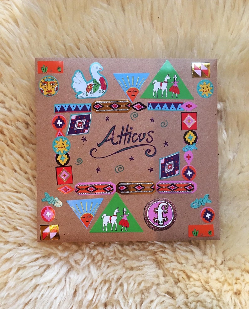 Pu&ograve; includere: Un sacchetto regalo di carta marrone con adesivi colorati. Gli adesivi raffigurano un uccello, un lama, un sole, uno schema geometrico e la parola "Atticus".